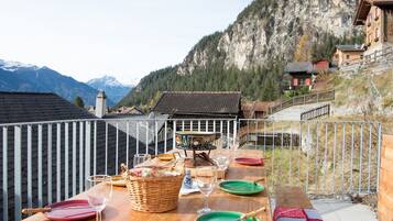 Une table à manger installée à l’extérieur, avec vue sur les montagnes, et entourée d’une rambarde en métal.