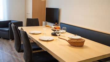 Uma sala de jantar com uma mesa comprida, cadeiras, uma televisão e uma cesta.