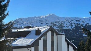 Een modern gebouw met een schuin dak, grote ramen en een besneeuwd landschap met bergen op de achtergrond.