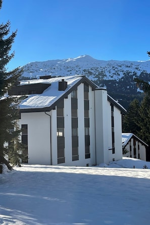 A modern building with a sloped roof, large windows, and a snow-covered landscape with mountains in the background. - 1619 Sundroina Prada C by Interhome (Lenzerheide)