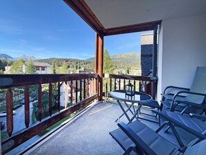 Un balcone con vista su una montagna e una strada. Si vedono un tavolo e delle sedie.