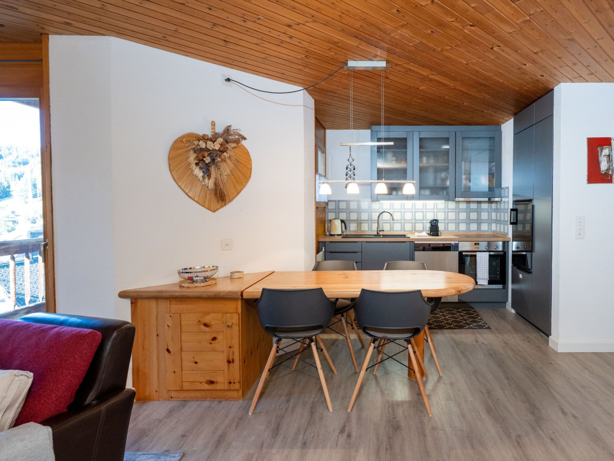 Una cucina moderna con mobili in legno, un tavolo da pranzo con sedie e una decorazione a forma di cuore al muro.