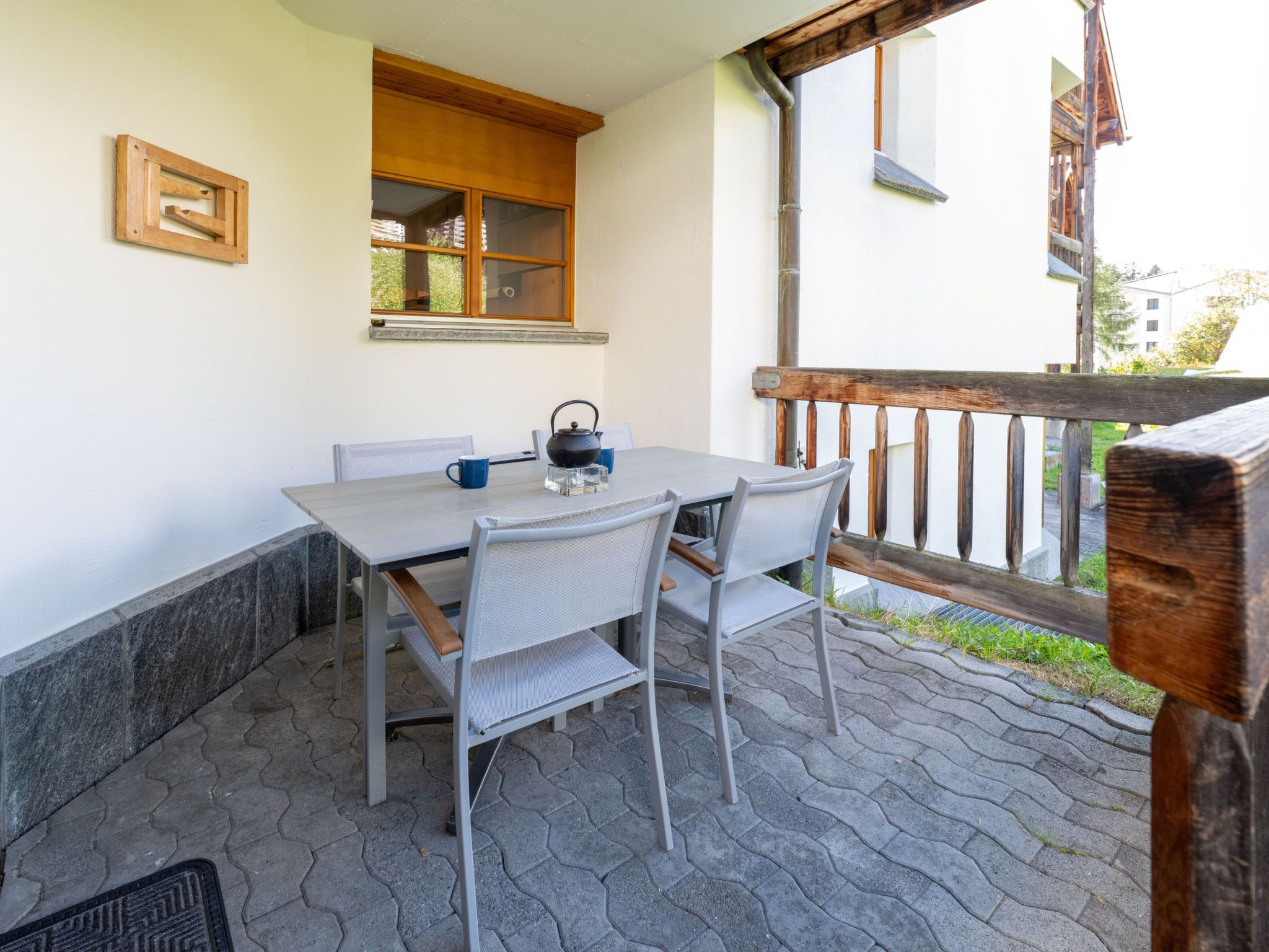 Eine Terrasse mit Tisch, Stühlen, einem Fenster und einem Holzgeländer.