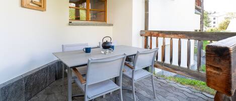 Eine Terrasse mit Tisch, Stühlen, einem Fenster und einem Holzgeländer.