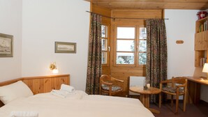 A room with a bed, two chairs, a table, a window with curtains, and a bookshelf. - 1609 Schweizerhof 604 by Interhome (Lenzerheide)