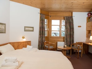A room with a bed, two chairs, a table, a window with curtains, and a bookshelf. - 1609 Schweizerhof 604 by Interhome (Lenzerheide)