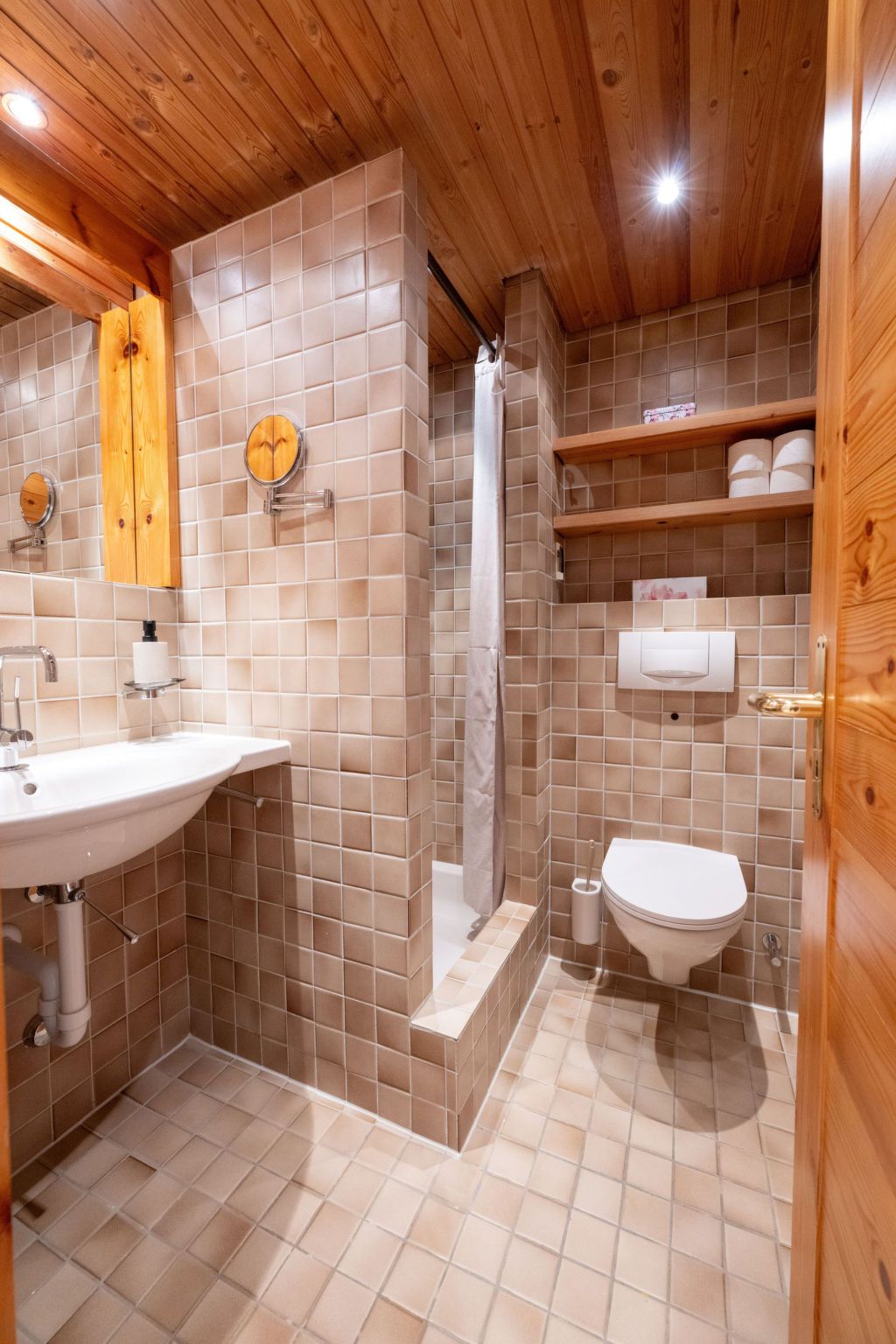 Ein Badezimmer mit Holzbalkendecke, einem Waschbecken, einer Toilette und einer Duschkabine.
