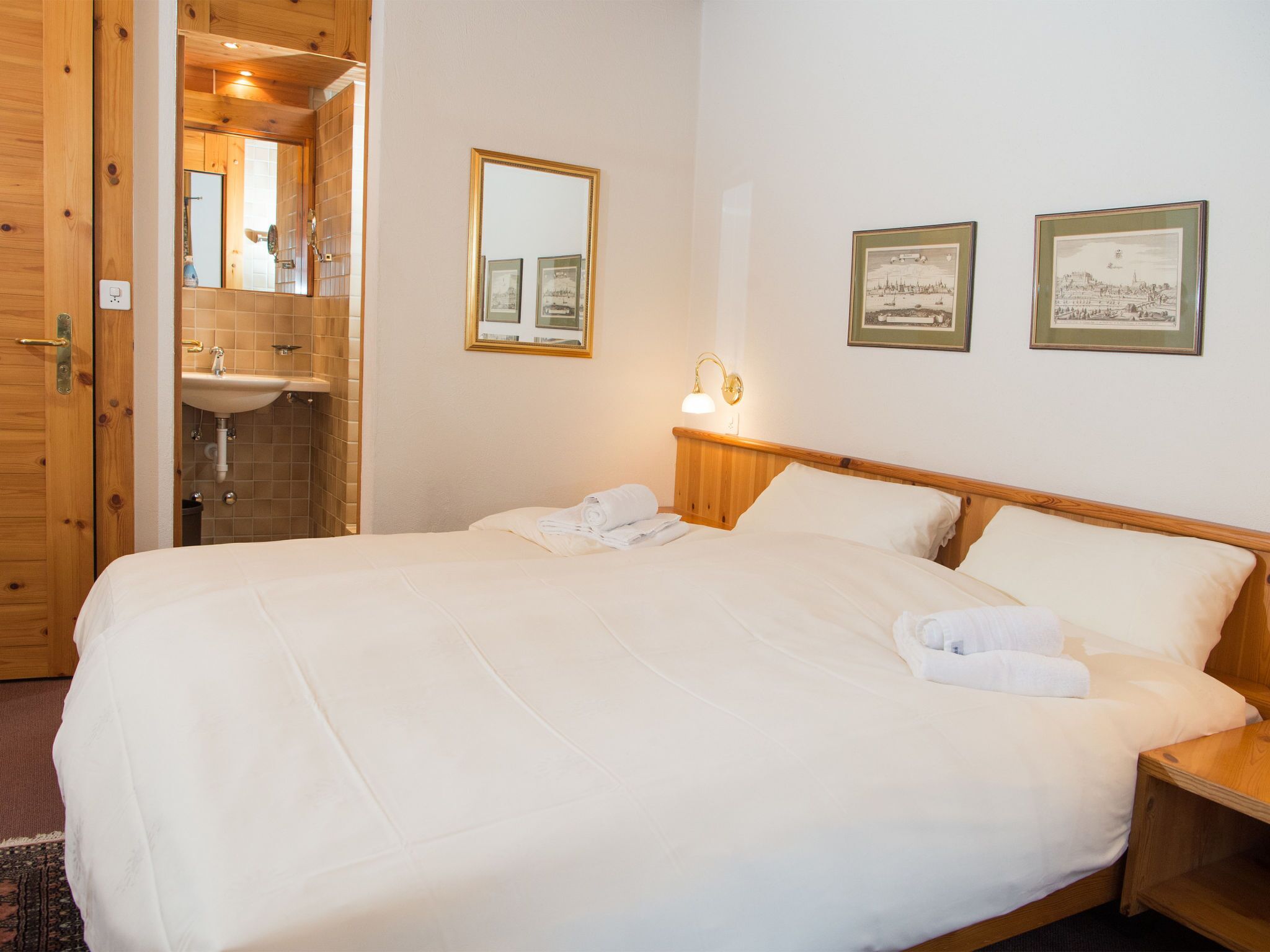 Ein Hotelzimmer mit einem großen Bett, einem Holzkopfstück, einem Nachttisch mit Lampe, einem Spiegel und zwei gerahmten Bildern an der Wand.