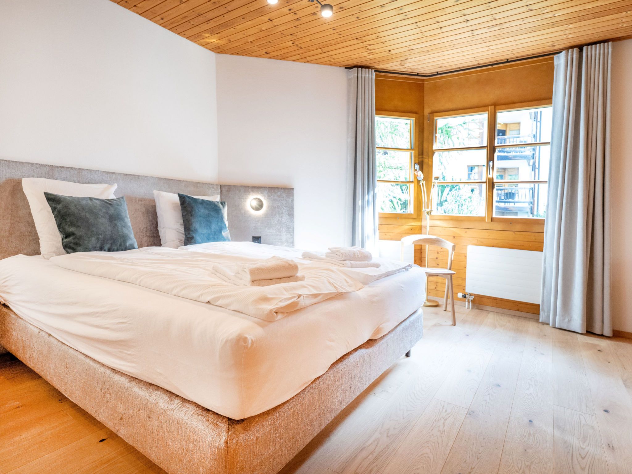 Ein Schlafzimmer mit einem großen Bett, einem Nachttisch, einem Sessel und einem Fenster mit Vorhängen.