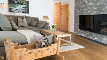 Ein modernes Wohnzimmer mit einer Couch, einem Hundebett aus Holz, einem Kamin und einer Steinwand.