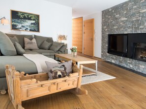 A modern living room with a sofa, a wooden dog bed, a fireplace, and a stone wall. - 1907 Valmala by Interhome (Lantsch)