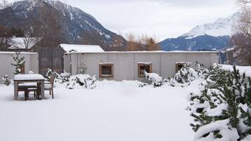A snow-covered outdoor area with a table and chairs, a wooden fence, and a building with windows.