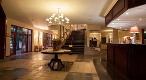 A spacious lobby with a grand staircase, a reception desk, and a chandelier. - The Wilderness Hotel (Wilderness)