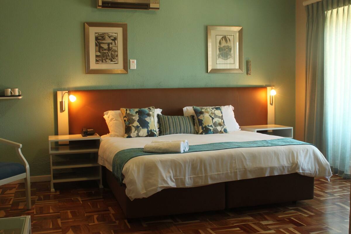 A neatly arranged hotel room with a large bed, a bedside table, a chair, and a wall-mounted lamp.