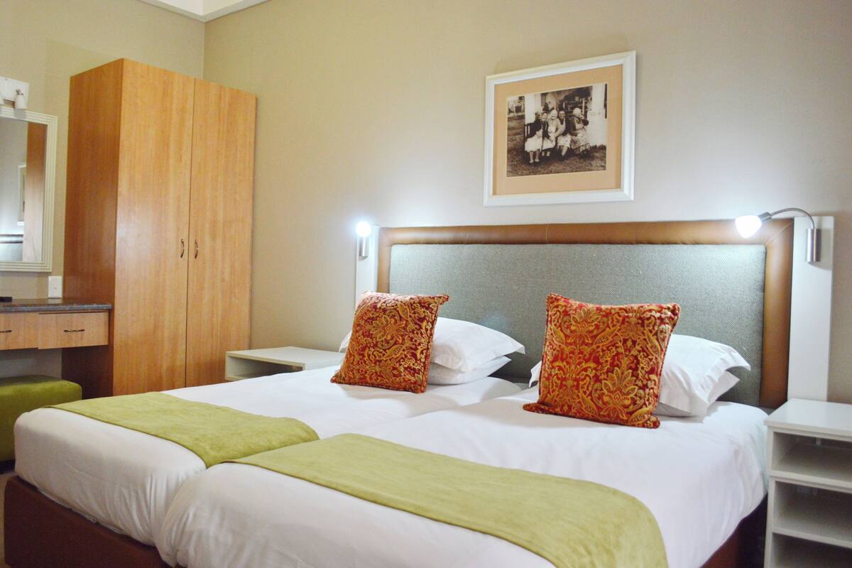 A hotel room with a large bed, two pillows, a nightstand, a mirror, a wardrobe, and a framed photo on the wall.