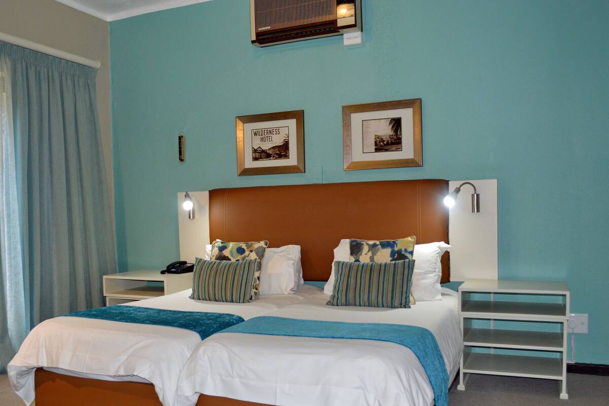 A double bed with two pillows, a nightstand, a lamp, and a framed picture on the wall.