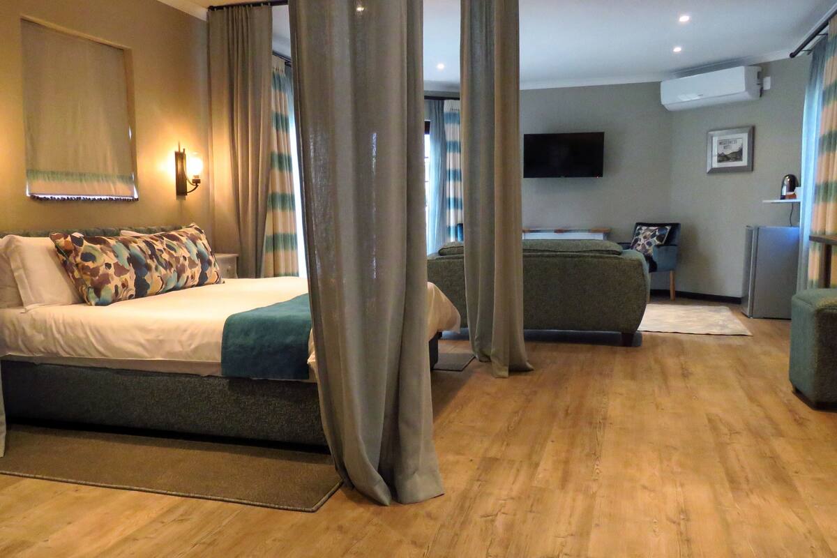 A hotel room with a bed, a sofa, a TV, and a refrigerator.