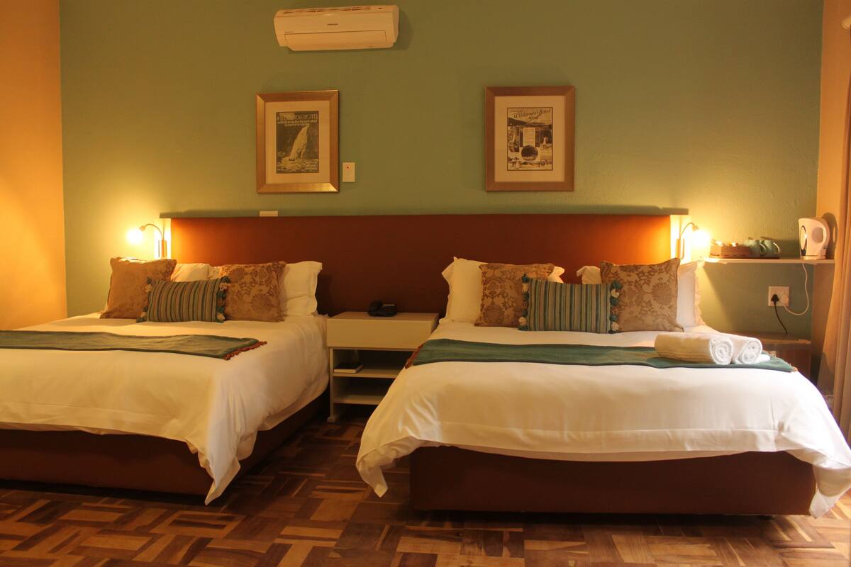 A hotel room with two beds, a wooden floor, and framed pictures on the wall.