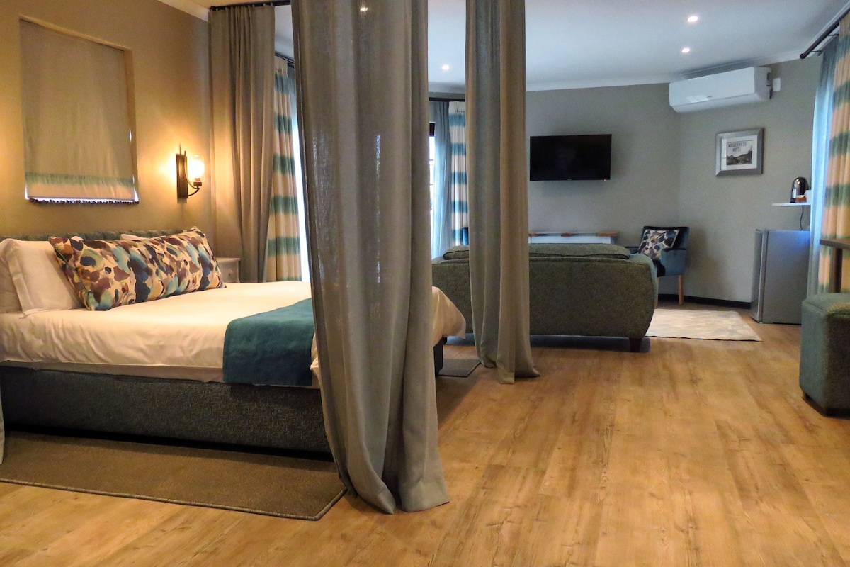 A hotel room with a bed, a sofa, a TV, and a refrigerator.