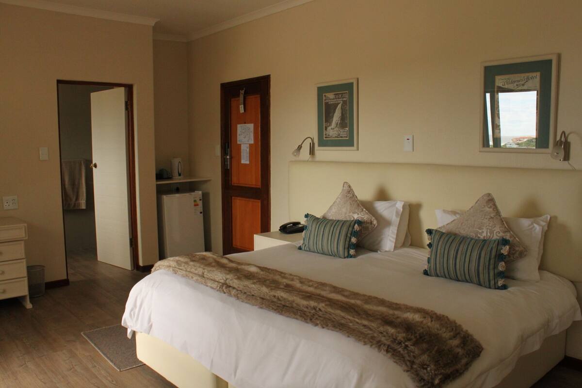 A hotel room with a large bed, a nightstand, a desk, and a mirror.