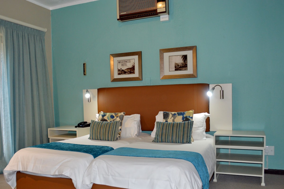 A double bed with two pillows, a nightstand, a lamp, and a framed picture on the wall.