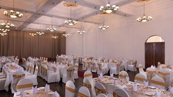 A banquet hall with round tables set for dining, white chairs with gold sashes, and chandeliers hanging from the ceiling.