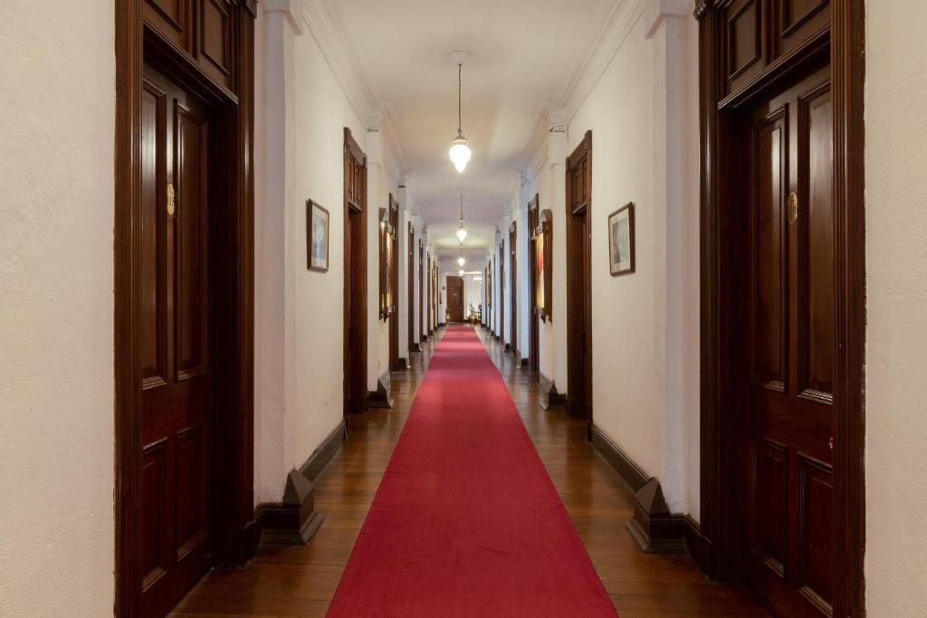 Un long couloir bordé de portes en bois de chaque côté et recouvert d’un tapis rouge.