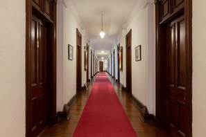 Un long couloir bordé de portes en bois de chaque côté et recouvert d’un tapis rouge.
