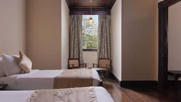 A hotel room with two beds, a window with curtains, a wooden ceiling, and a small table with chairs.