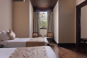 Una habitación de hotel con dos camas, una ventana con cortinas, techo de madera y una pequeña mesa con sillas.