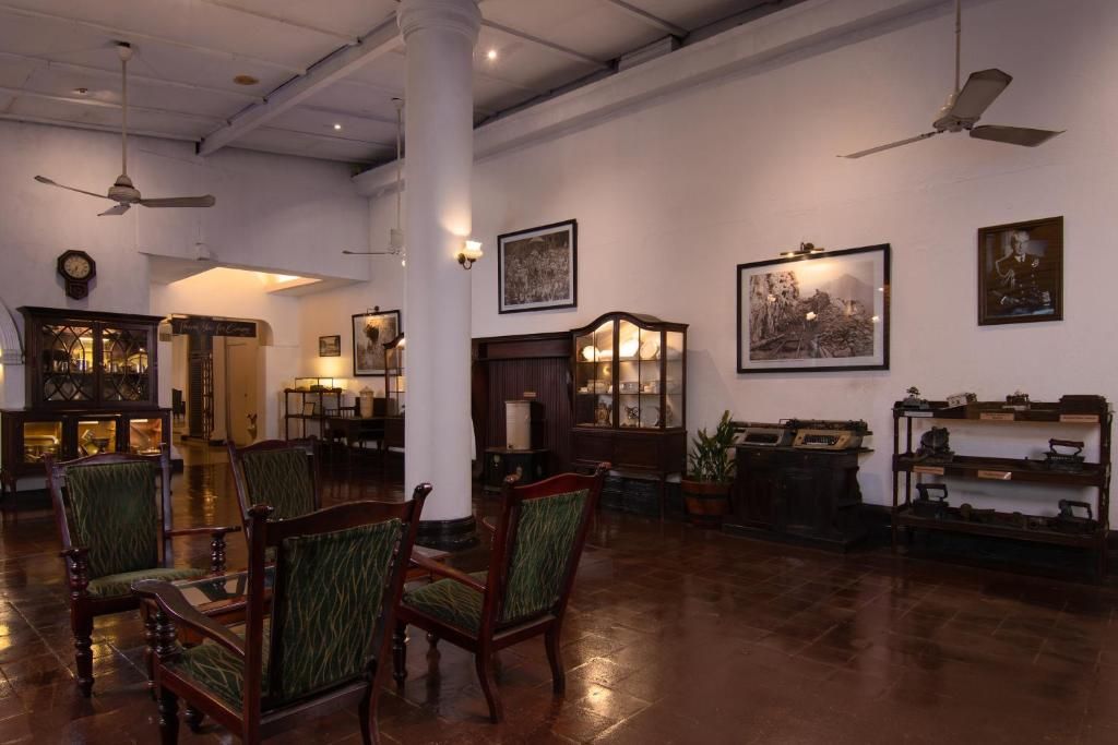 A spacious lobby with wooden chairs, a large pillar, ceiling fans, and framed artwork on the walls.