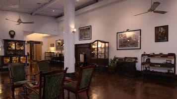 A spacious lobby with wooden chairs, a large pillar, ceiling fans, and framed artwork on the walls.