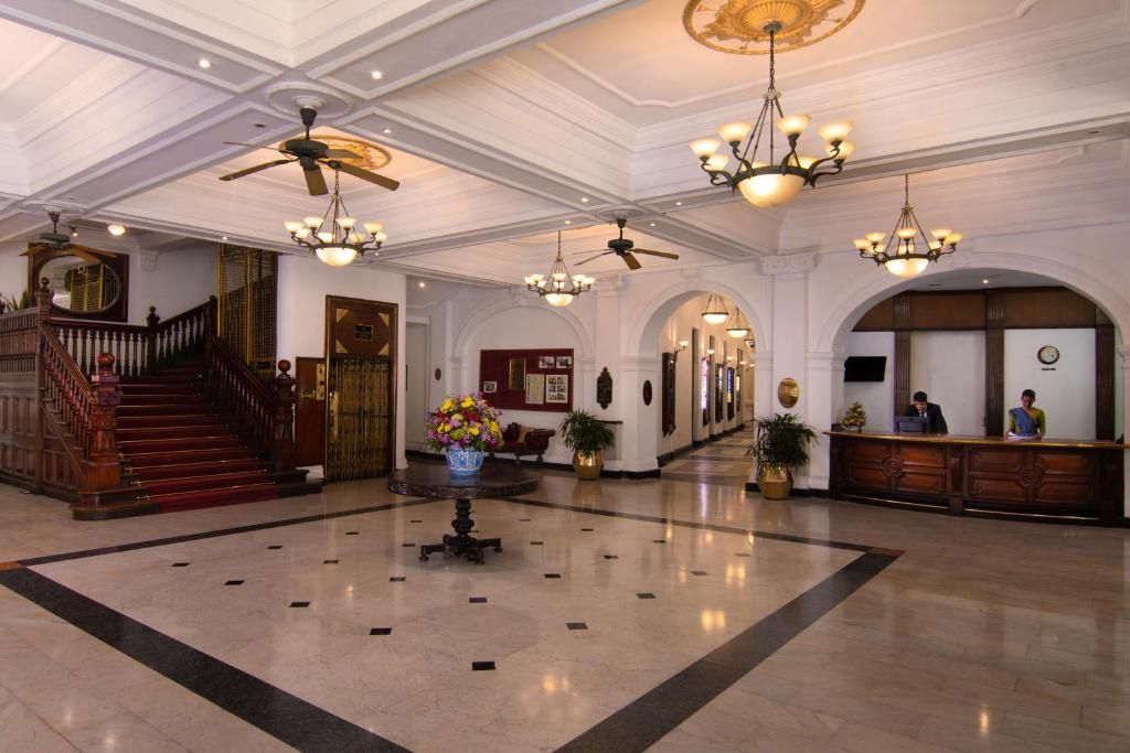 A spacious lobby with a grand staircase, multiple chandeliers, and a reception desk.