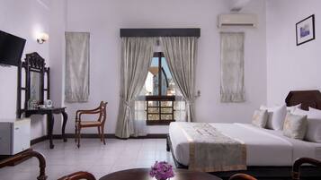 A hotel room with a bed, a desk with a computer, a chair, a table with a vase, and a window with curtains.