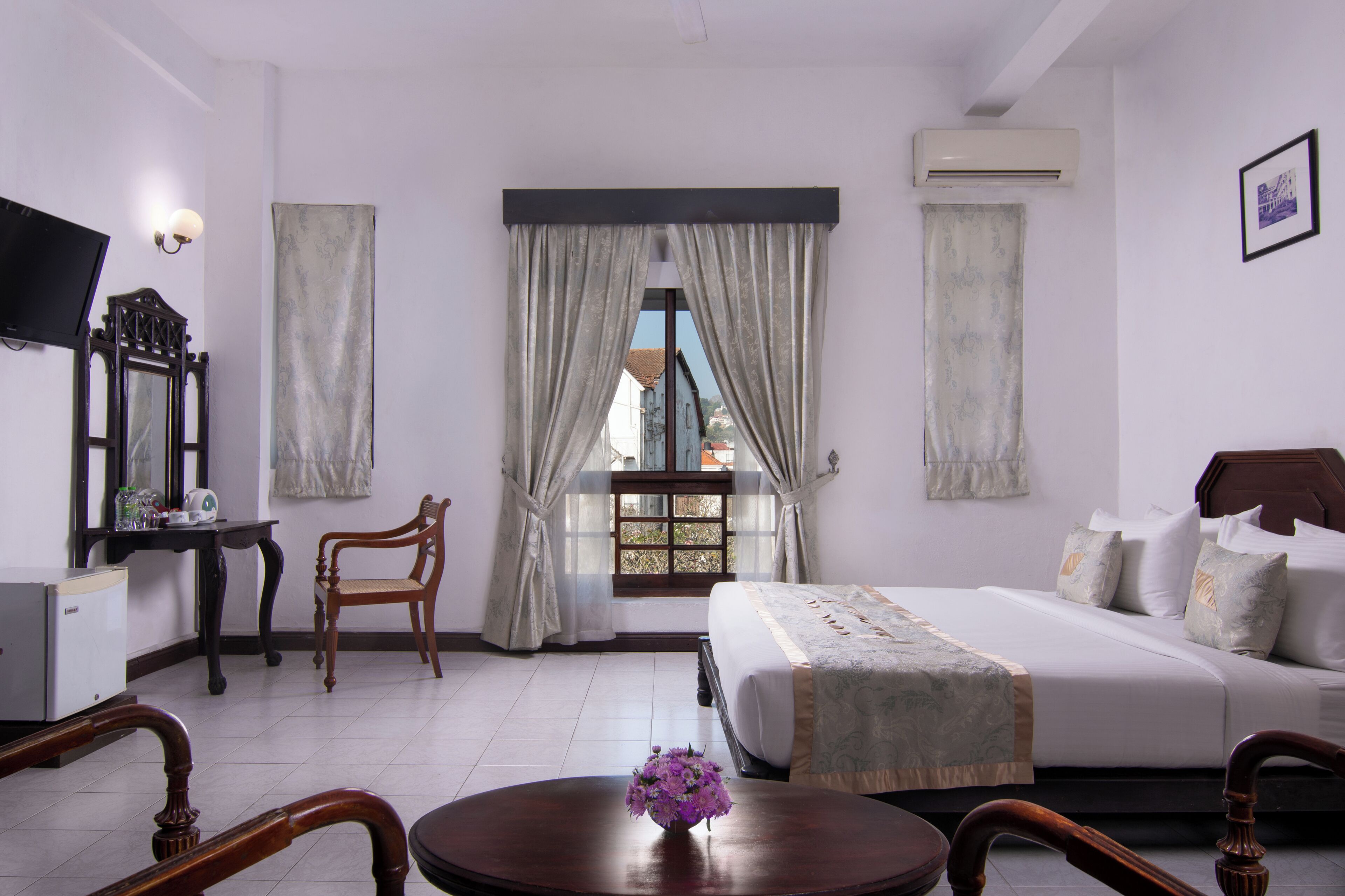 A hotel room with a bed, a desk, a chair, a television, and a window with curtains.