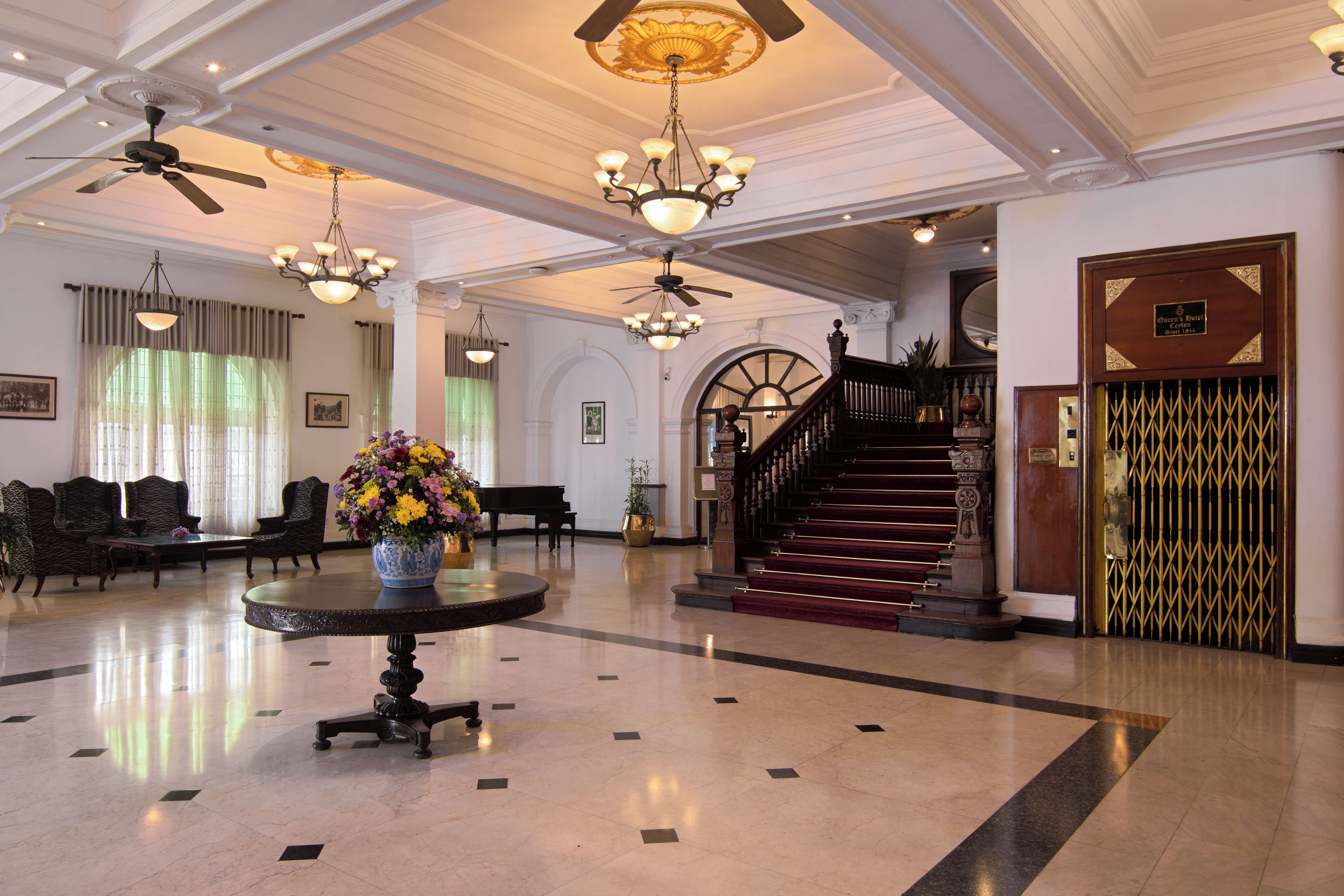 Un lobby imponente con techo alto, candelabros, un piano y una escalera que lleva a un piso superior.