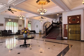 Un lobby imponente con techo alto, candelabros, un piano y una escalera que lleva a un piso superior.