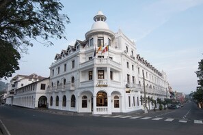 Un edificio blanco con una cúpula central y varios balcones, identificado como el Hotel Queen's.