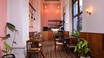 Interior de restaurante com mesas e cadeiras de madeira, área de bar e plantas em vasos.