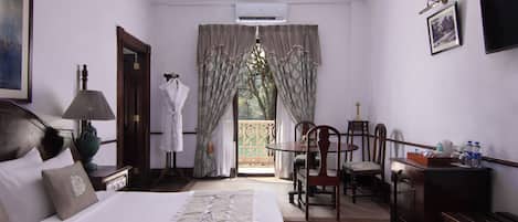 A hotel room with a bed, a desk, a chair, a TV, and a window with curtains.