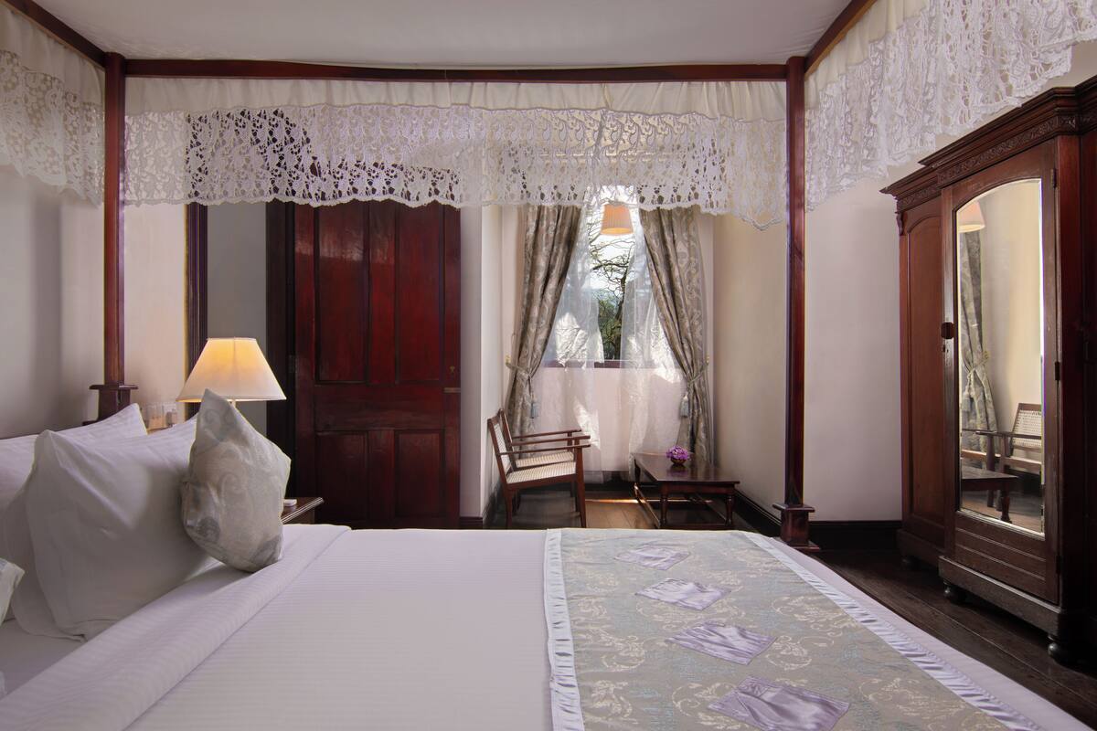 Camera d'albergo ordinata con un letto grande, un comodino in legno, una scrivania con una lampada e una sedia.