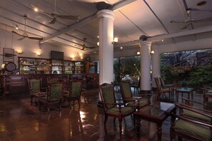 Una zona de bar con sillas y mesas de madera, un televisor y vistas a un espacio exterior con plantas.