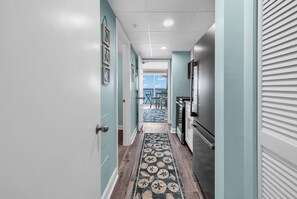 A hallway with a patterned rug, a refrigerator, and a view to a balcony. - Beachfront, Penthouse, Views, Amenities, Location! (Myrtle Beach)