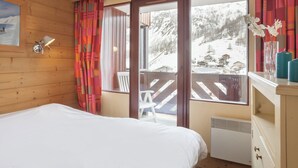 A hotel room with a bed, a window with a view of a snowy mountain, a wooden wall, and a white radiator. - Residence Pierre et Vacances Balcons de Bellevarde (Val-d'Isere)