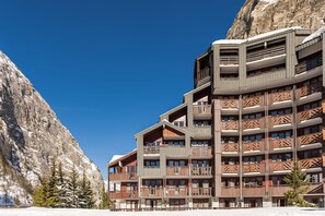A multi-story hotel with balconies, set against a mountainous backdrop.
