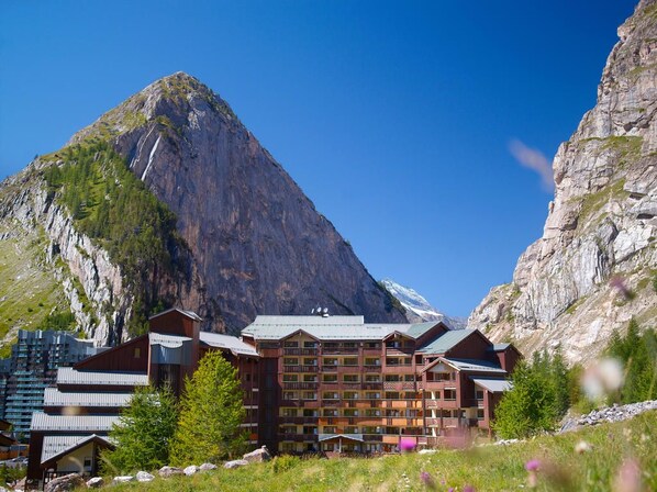 A mountain lodge with multiple floors, balconies, and a view of a steep mountain.