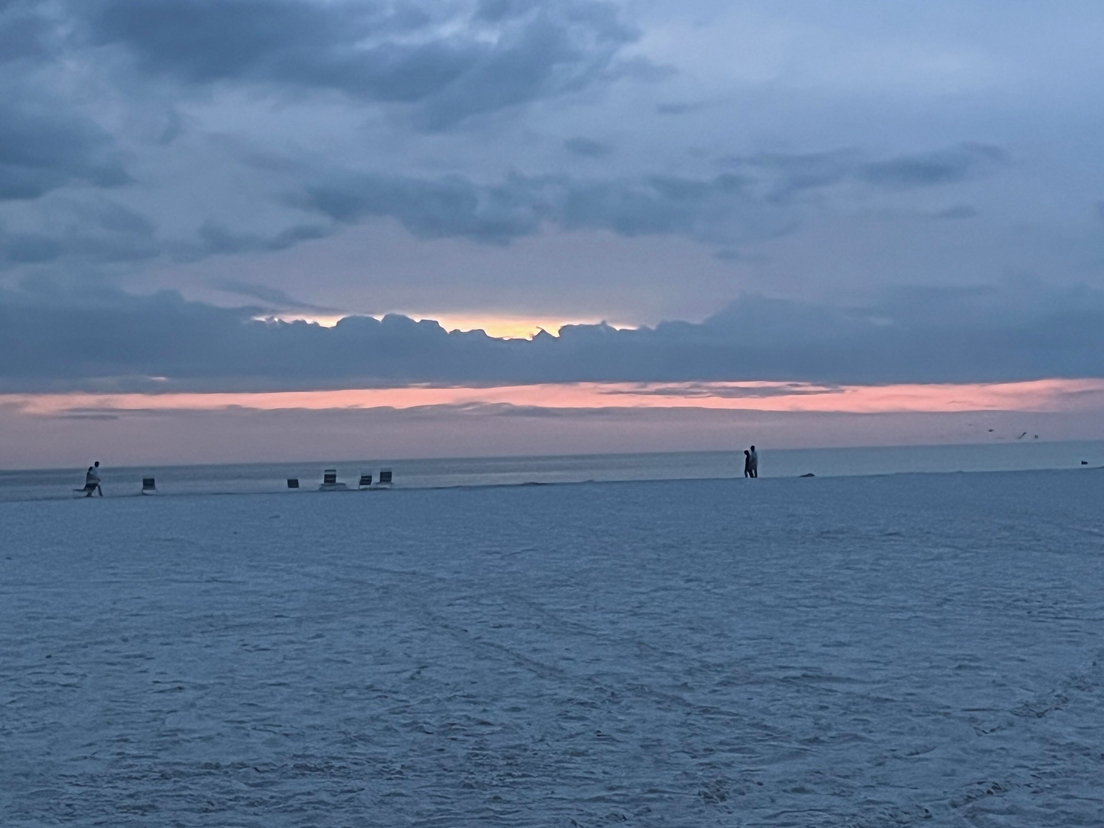Una spiaggia al tramonto, con mare calmo e montagne in lontananza.