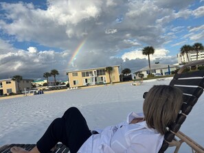 Ein Strand mit Regenbogen, Palmen und Gebäuden im Hintergrund.