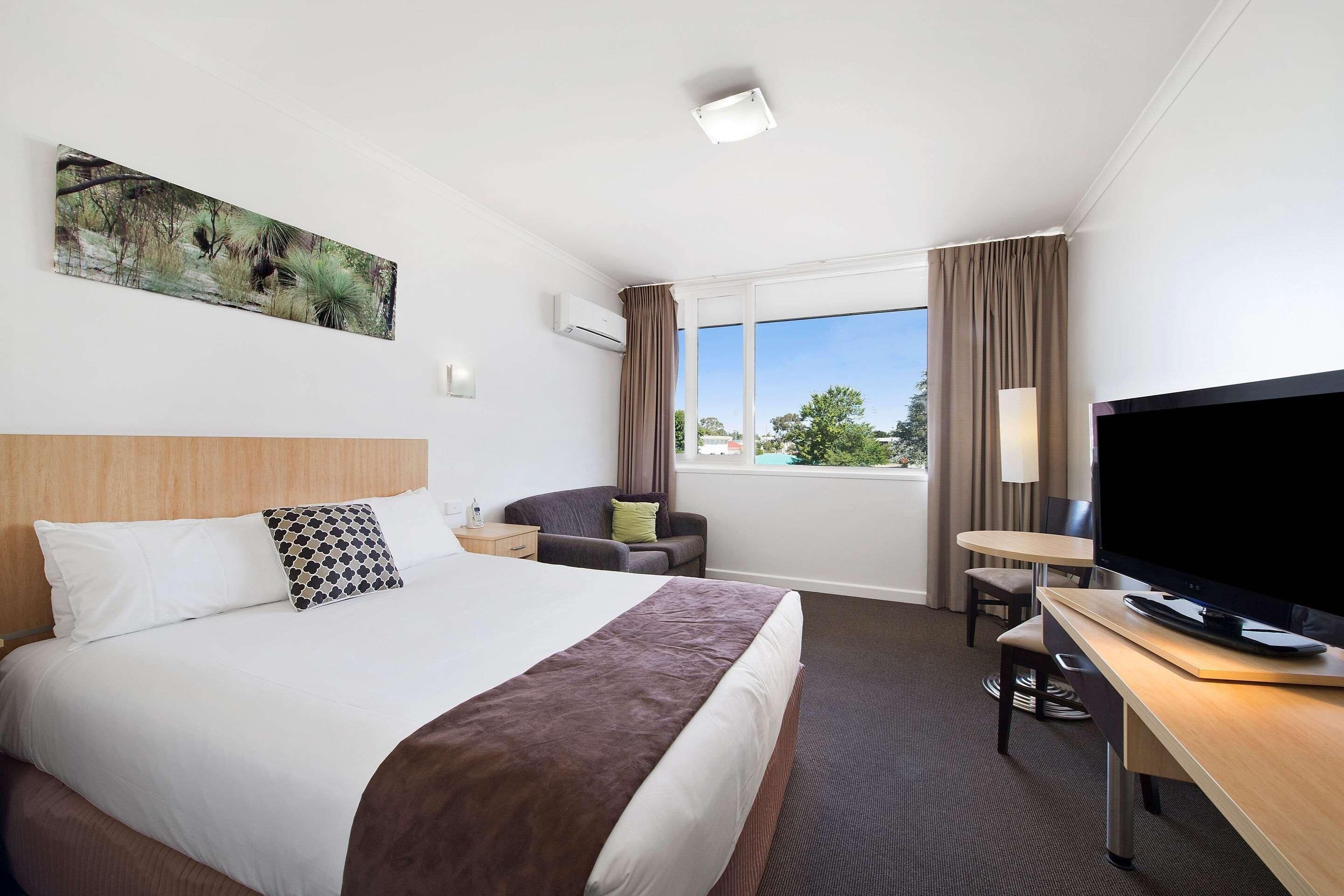 A hotel room with a large bed, a desk with a TV, a chair, and a window with curtains.