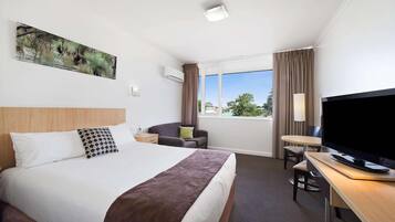 A hotel room with a large bed, a desk with a TV, a chair, and a window with curtains.